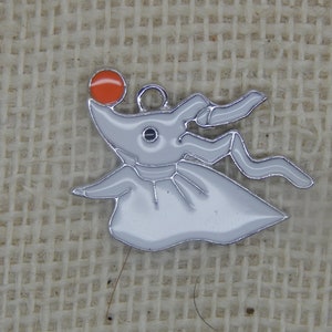 May include: White metal charm of a ghost character with an orange ball on top of its head. The ghost has a long, flowing tail and a single eye.