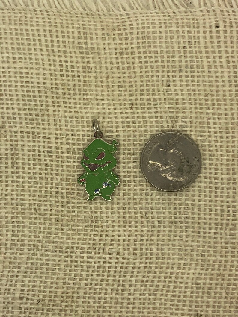May include: Green Grinch character charm with a red heart and a blue flower. The charm is made of metal and has a shiny finish. The charm is about the size of a US quarter.