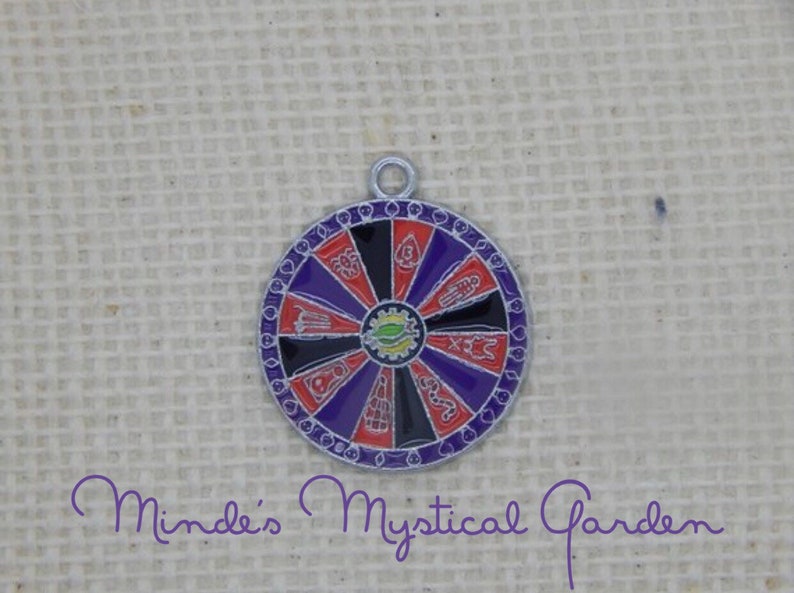 May include: A silver charm in the shape of a wheel of fortune with red, black, and purple sections. Each section has a different symbol, including a hand, a snake, a spider, and a skull.