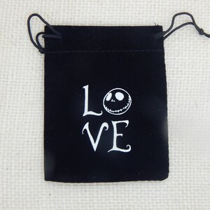 May include: Black velvet drawstring bag with white lettering that says "LOVE" and a white Jack Skellington face.