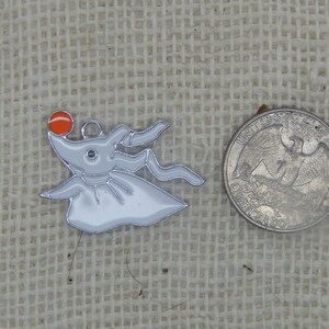 May include: A silver charm featuring a white ghost with a red nose and a black eye. The charm is about the size of a US quarter.