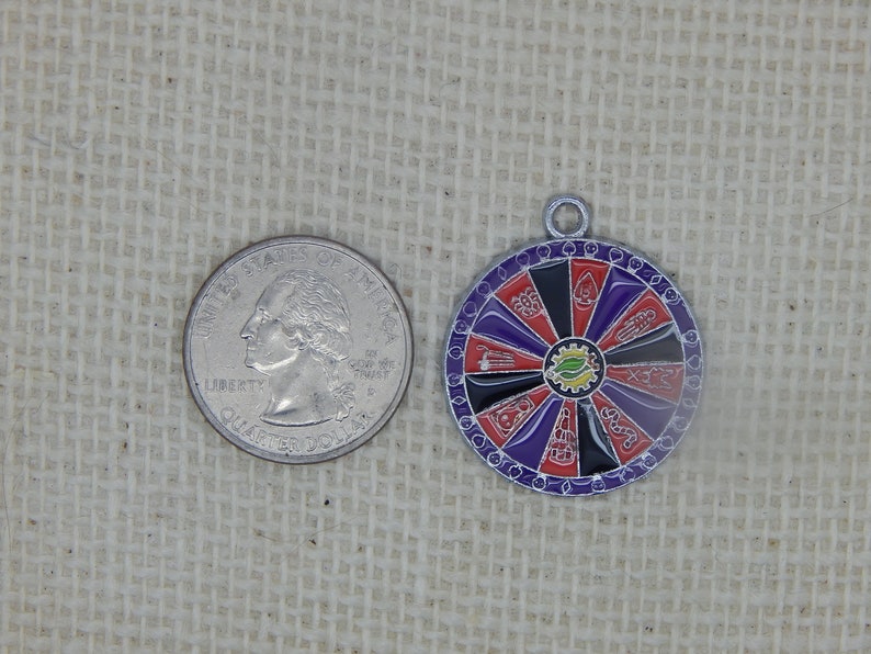 May include: A silver charm with a colorful wheel of fortune design. The wheel has red, black, purple, and yellow sections with various symbols. The charm is about the size of a US quarter.