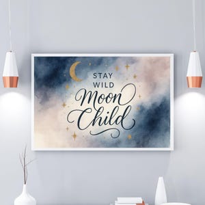 May include: A framed art print with the words "Stay Wild Moon Child" in elegant script. The background features a watercolor design in shades of blue, pink, and gold, with a crescent moon and stars.