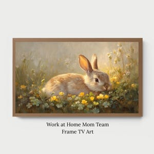 May include: A framed print depicting a rabbit amidst yellow flowers. The rabbit has light brown fur and long ears. The artwork is rendered in a soft, painterly style, with a warm colour palette and a focus on natural light.