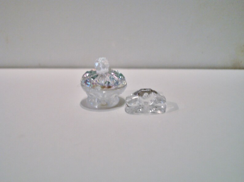 Peut inclure: Une bo&icirc;te &agrave; bijoux en verre transparent avec un bouton d&eacute;coratif sur le dessus. La bo&icirc;te est en verre transparent avec une finition iris&eacute;e.