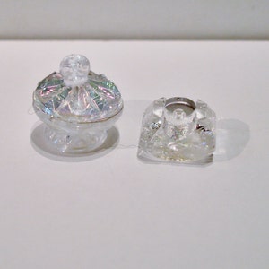 Peut inclure: Deux pi&egrave;ces d&eacute;coratives en verre transparent. L'une est un petit bol rond et iridescent avec un bouton sur le dessus. L'autre est une pi&egrave;ce carr&eacute;e en verre transparent avec un petit trou au centre.