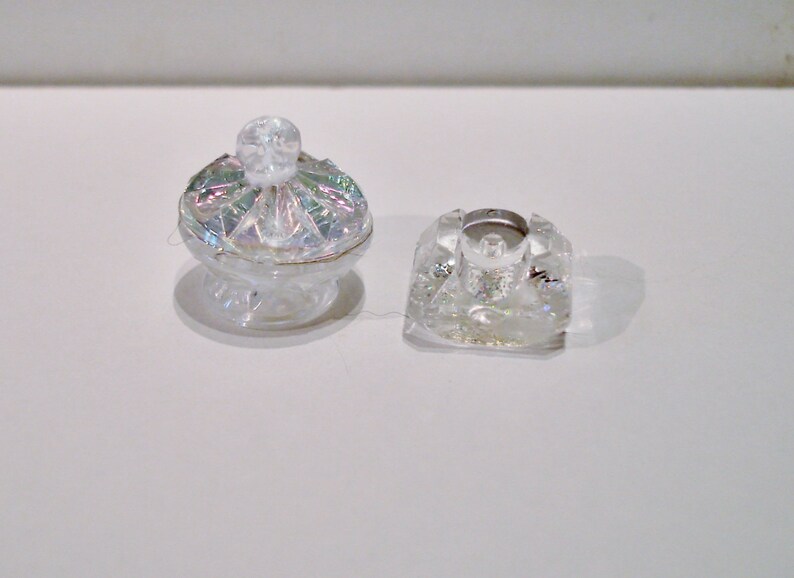 Peut inclure: Deux pi&egrave;ces d&eacute;coratives en verre transparent. L'une est un petit bol rond et iridescent avec un bouton sur le dessus. L'autre est une pi&egrave;ce carr&eacute;e en verre transparent avec un petit trou au centre.