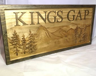 May include: A wooden sign with the words "Kings Gap" carved into it. The sign features a carved mountain scene with trees.