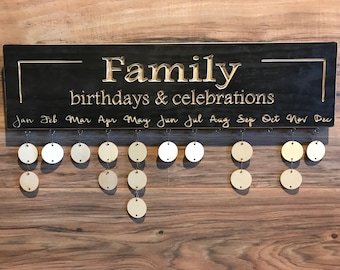 May include: A black wooden sign with the words "Family birthdays & celebrations" engraved in gold. The sign has 12 hooks for hanging wooden circles, one for each month of the year.