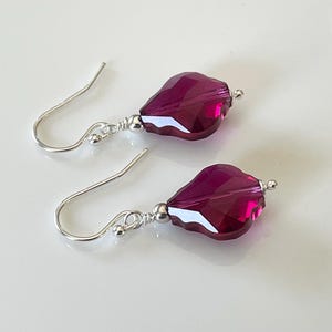 May include: A pair of silver dangle earrings with a deep pink faceted crystal drop on each earring.