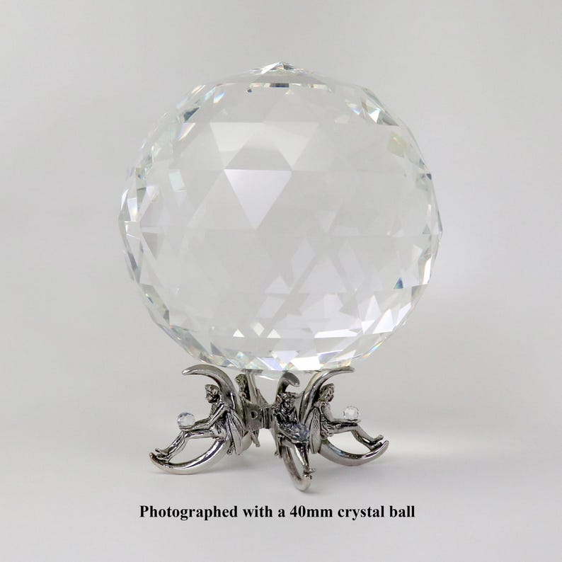 Puede incluir: Una bola de cristal transparente y facetada, de aproximadamente 4 cm de di&aacute;metro, se encuentra sobre un soporte decorativo de metal plateado. El soporte presenta tres figuras. El texto en la parte inferior dice: Photographed with a 40mm crystal ball.