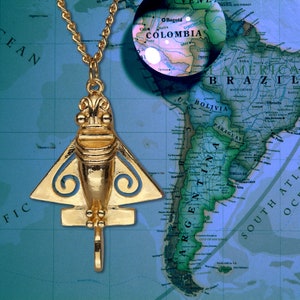 May include: A gold-colored pendant necklace featuring a stylized airplane design with blue accents. The pendant is set against a map of South America.
