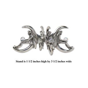 Puede incluir: Pinza de pelo de metal plateado con tres figuras de hadas. Cada hada sostiene una bola de cristal transparente. La pinza mide 3,8 cm de alto por 8,9 cm de ancho.