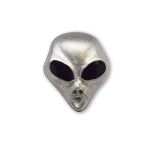 May include: A silver alien head pin with black eyes. The alien has a wide mouth and a textured surface.