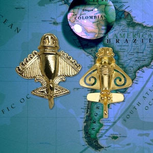 May include: Two gold-colored pre-Columbian airplane artifacts are displayed against a map of South America. The artifacts have wings and intricate details. The map shows the country of Colombia under a magnifying glass.