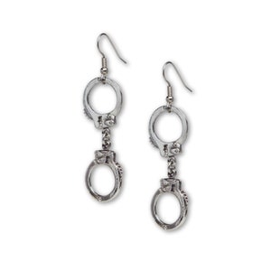 May include: Silver-toned metal earrings featuring a handcuff design. Each earring has a hook for pierced ears, with a small handcuff charm suspended below a larger one. The earrings are detailed with rivets and a textured finish.