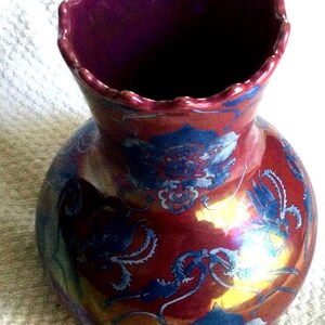 Peut inclure: Un vase d&eacute;coratif avec un corps bulbeux et un bord festonn&eacute;. Le vase est principalement rouge avec des motifs floraux bleus et des reflets iris&eacute;s. L'int&eacute;rieur est de couleur violet fonc&eacute;.