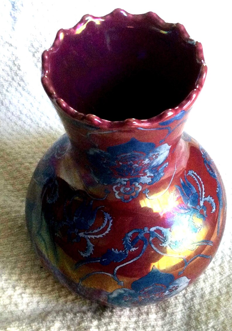 Peut inclure: Un vase d&eacute;coratif avec un corps bulbeux et un bord festonn&eacute;. Le vase est principalement rouge avec des motifs floraux bleus et des reflets iris&eacute;s. L'int&eacute;rieur est de couleur violet fonc&eacute;.