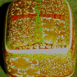 May include: Rectangular decorative box with a floral design. The box features a gold leaf pattern on a cream background, with red and green accents. The box has a rounded top and sides.