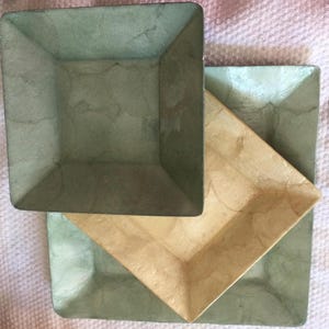 May include: Three square trays, one green, one beige, and one larger green tray. The trays are made of a textured material that resembles paper.