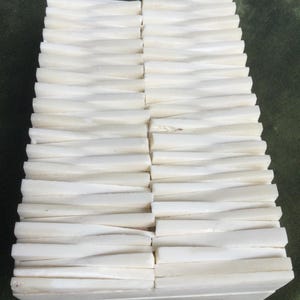 May include: A stack of off-white, rectangular tiles with a wavy, textured design. The tiles are arranged in a grid pattern, creating a repeating wave effect. The overall aesthetic is clean and modern.