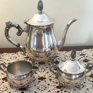 May include: A silver tea set with a teapot, creamer, and sugar bowl. The set has ornate details and a polished finish.
