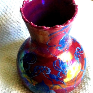 Peut inclure: Un vase d&eacute;coratif avec un bord festonn&eacute; et un corps bulbeux. Le vase est principalement rouge avec des motifs floraux bleus et des reflets iris&eacute;s. Le vase a une forme unique et une finition brillante.