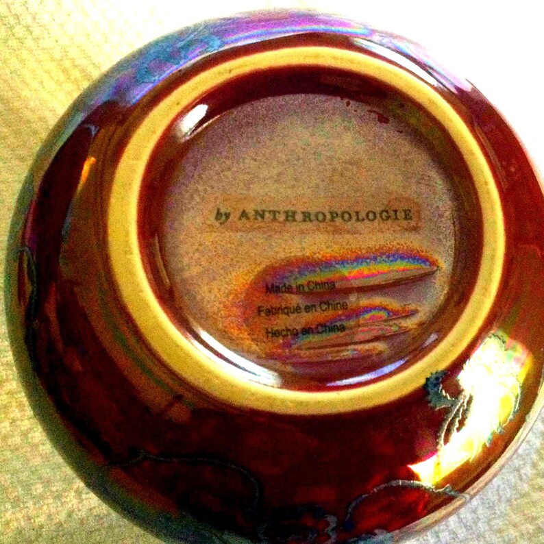 Peut inclure: Un bol en c&eacute;ramique avec une finition brillante et iris&eacute;e. L'ext&eacute;rieur du bol est d'un brun rouge&acirc;tre profond, passant &agrave; un bord jaune dor&eacute; plus clair. La base int&eacute;rieure porte les mentions "by ANTHROPOLOGIE" et "Made in China".