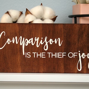 Puede incluir: Un letrero de madera con el texto "Comparison is the thief of joy" en letras blancas sobre un fondo marr&oacute;n.