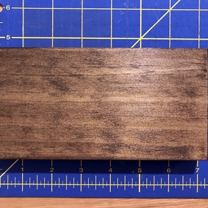 Puede incluir: Un letrero de madera marr&oacute;n oscuro con un acabado liso y ligeramente brillante. El letrero es rectangular y tiene un patr&oacute;n de veta de madera natural.
