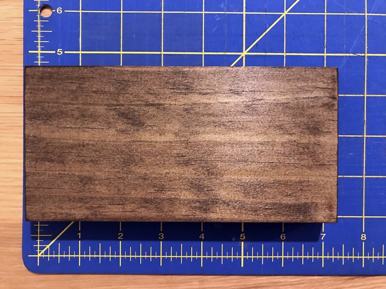Puede incluir: Un letrero de madera marr&oacute;n oscuro con un acabado liso y ligeramente brillante. El letrero es rectangular y tiene un patr&oacute;n de veta de madera natural.