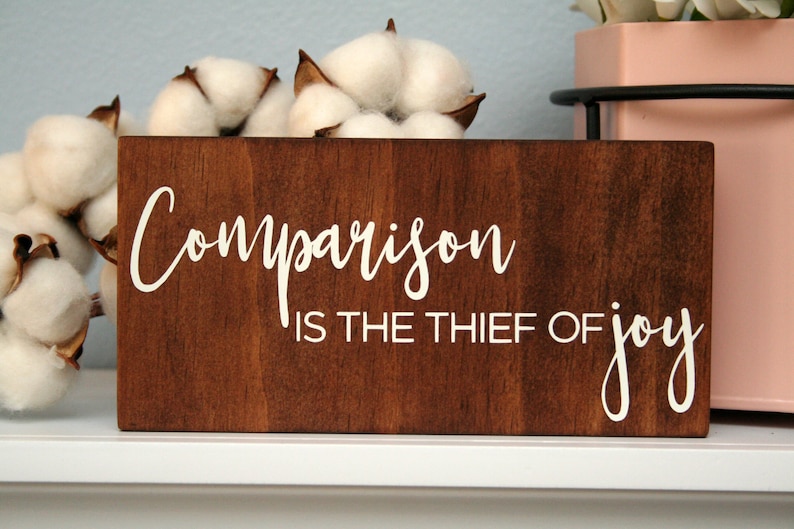 Puede incluir: Un letrero de madera con el texto "Comparison is the thief of joy" en letras blancas sobre un fondo marr&oacute;n.