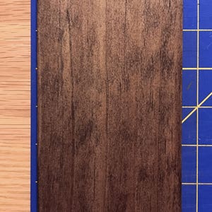 Puede incluir: Un primer plano de una tabla de madera marr&oacute;n oscuro con una superficie lisa y ligeramente texturizada. La tabla mide aproximadamente 7,6 cm de ancho y 10,2 cm de largo.