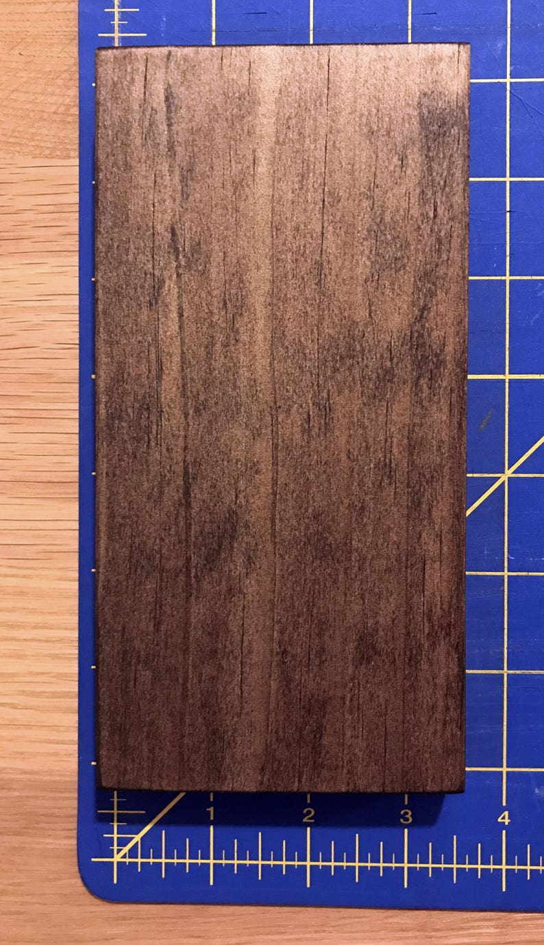 Puede incluir: Un primer plano de una tabla de madera marr&oacute;n oscuro con una superficie lisa y ligeramente texturizada. La tabla mide aproximadamente 7,6 cm de ancho y 10,2 cm de largo.