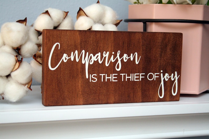 Puede incluir: Un letrero de madera con el texto "Comparison is the thief of joy" en letras blancas sobre un fondo marr&oacute;n.