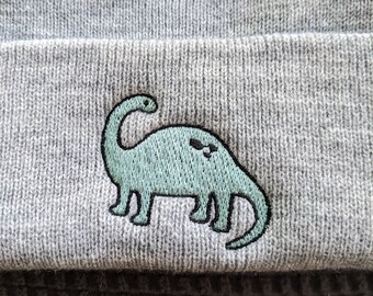 May include: Gray knitted beanie with a green embroidered dinosaur.