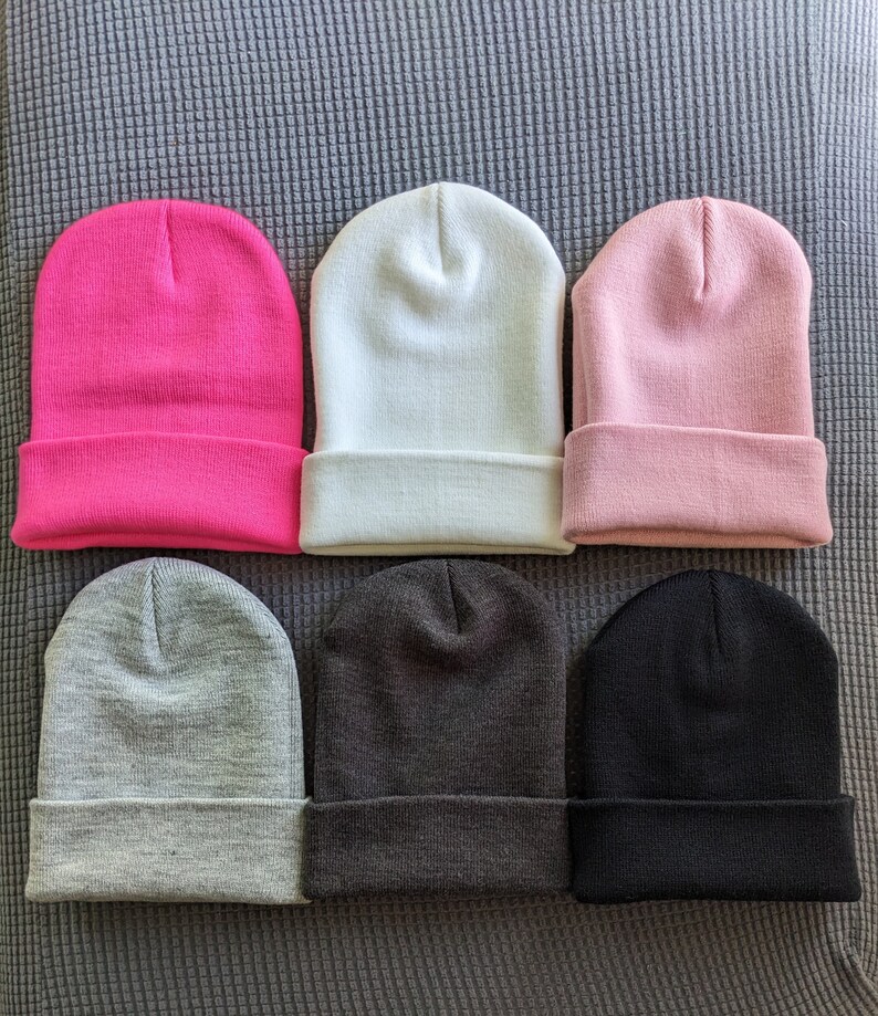 May include: Six beanies in different colors: pink, white, light pink, gray, dark gray, and black. The beanies are arranged in two rows of three.