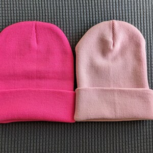 May include: Two knit beanies, one pink and one a darker shade of pink.