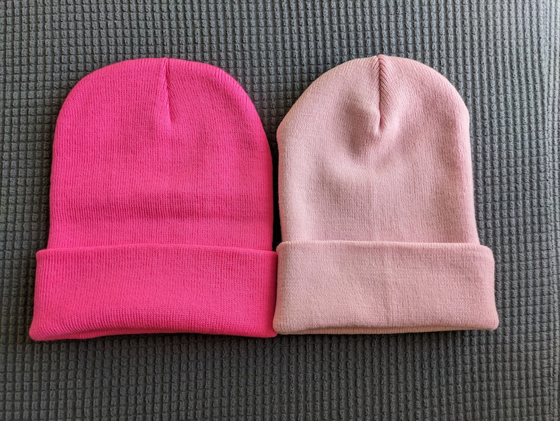 May include: Two knit beanies, one pink and one a darker shade of pink.