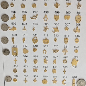 May include: A collection of 56 gold-colored metal charms with various designs, including animals, symbols, and shapes. The charms are arranged in rows and numbered from 488 to 543.