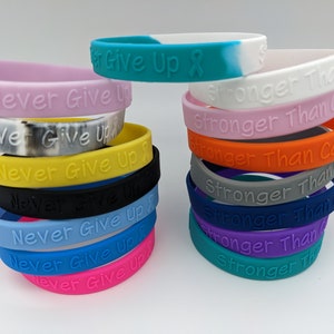 May include: A stack of colorful silicone wristbands with the phrases "Never Give Up" and "Stronger Than Cancer" printed on them.