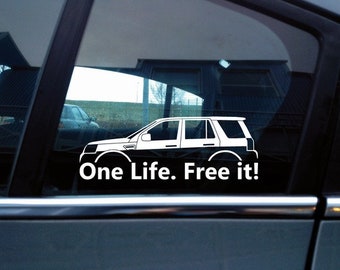 May include: A white vinyl decal applied to a car window featuring the silhouette of an SUV and the text One Life. Free it! in a clean sans-serif font. The design is monochromatic and displays the vehicle profile clearly.