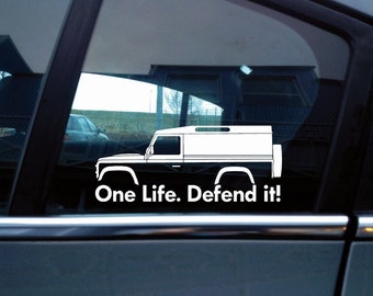 May include: A white vinyl decal applied to a car window, featuring the silhouette of a boxy off-road vehicle with a spare tire on the rear. Below the vehicle graphic, the text reads in a clean, sans-serif font: One Life. Defend it!