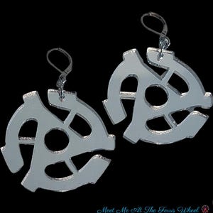 May include: Silver-colored earrings in the shape of 45 RPM record adapters. The earrings have a lever-back closure and are displayed against a black background. The text "Meet Me At The Ferris Wheel" is at the bottom.