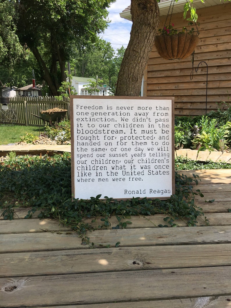 May include: A wooden sign with a white background and black text. The text reads: "Freedom is never more than one generation away from extinction. We didn't pass it to our children in the bloodstream. It must be fought for, protected, and handed on for them to do the same, or one day we will spend our sunset years telling our children, our children's children what it was once like in the United States where men were free." The text is signed "Ronald Reagan".