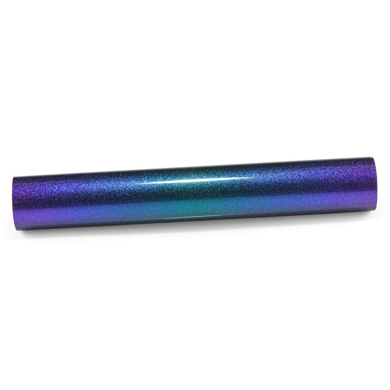 May include: A cylindrical roll of heat transfer vinyl featuring a smooth, glittery finish that transitions in color from a deep purple at the edges to a vibrant teal blue in the center, creating a seamless gradient effect across the surface.