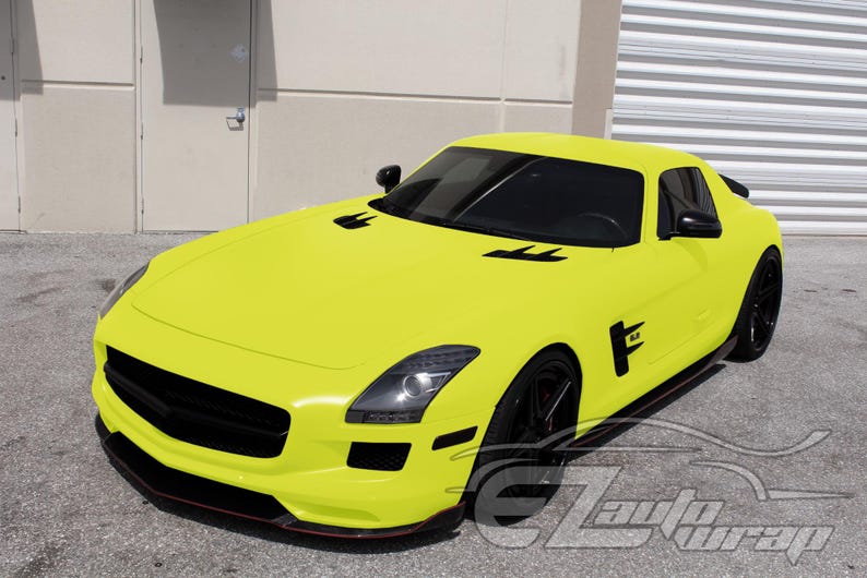 May include: A bright yellow sports car featuring a matte finish, black wheels, black side vents, and black front grille accents. The vehicle has a long hood, tinted windows, and a sleek aerodynamic body design with a low-profile front bumper.