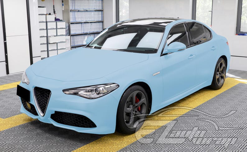 May include: A light blue sedan featuring a triangular front grille, sleek headlights, and dark grey wheels with visible red brake calipers. The vehicle has a black roof panel and a smooth, matte-finish exterior paint job, showcasing a modern design.