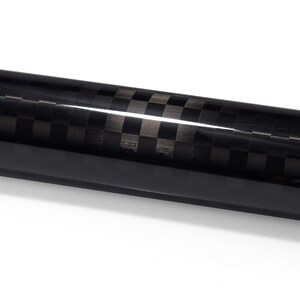 May include: A cylindrical rod featuring a glossy black and dark gray checkered carbon fiber pattern. The surface has a reflective finish with a distinct horizontal light highlight running across the length of the tube, showcasing the weave.