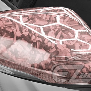 May include: A close-up of a car's side mirror with a pink and white camouflage pattern. The mirror is made of plastic and has a glossy finish.
